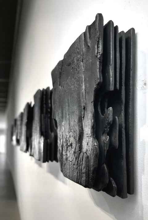 large black charred wood wall sculpture above sofa minimalist living room