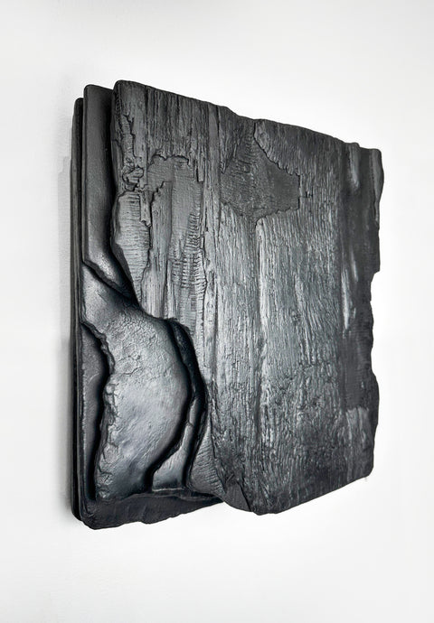 large black charred wood wall sculpture above sofa minimalist living room