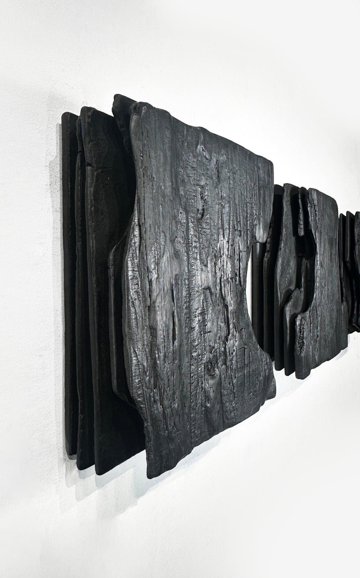 MORI — Charcoal Black, side view of stacked charred panels on white wall, relief depth