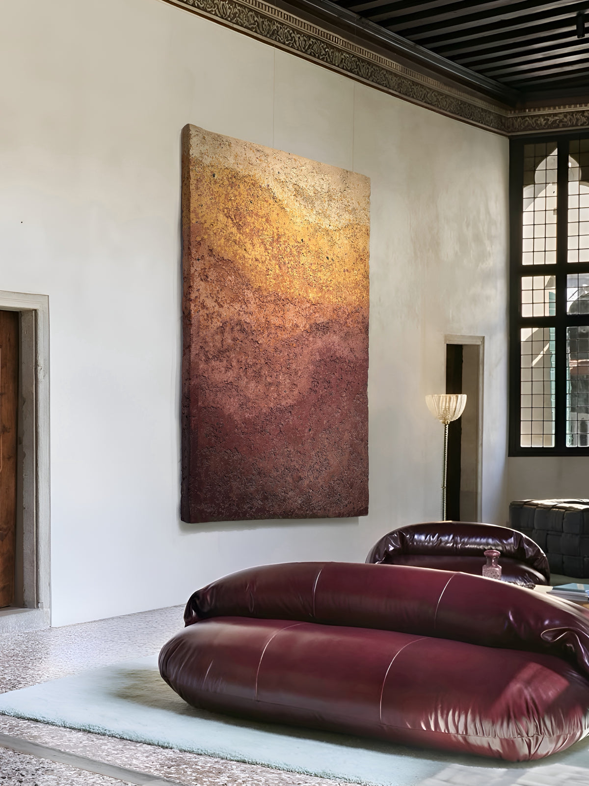 CHROMATERRA — tall panel in a historic interior with a carved ceiling frieze, above a burgundy leather sofa