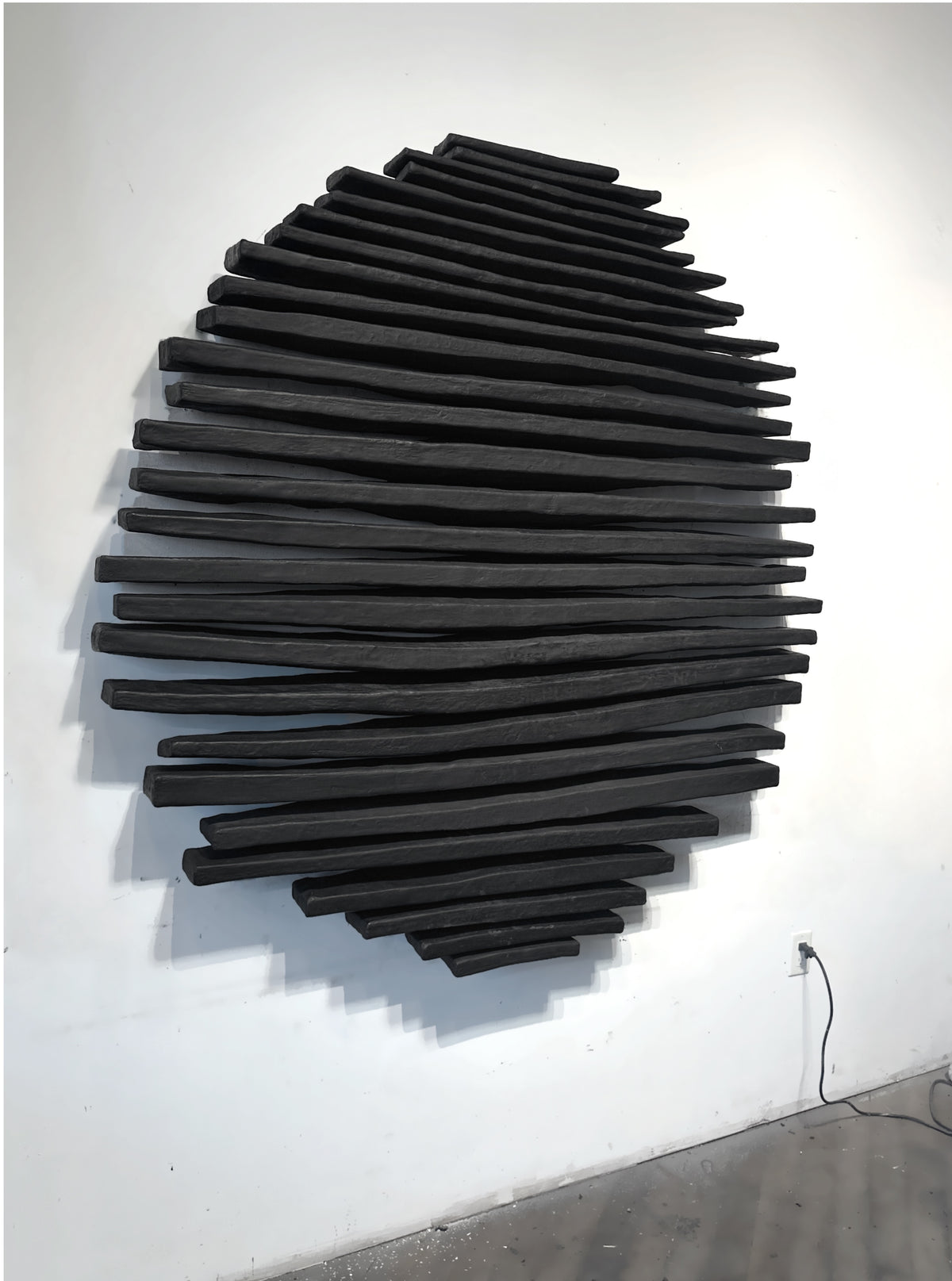 Black quilled wall sculpture on a bright white wall, seen straight on
