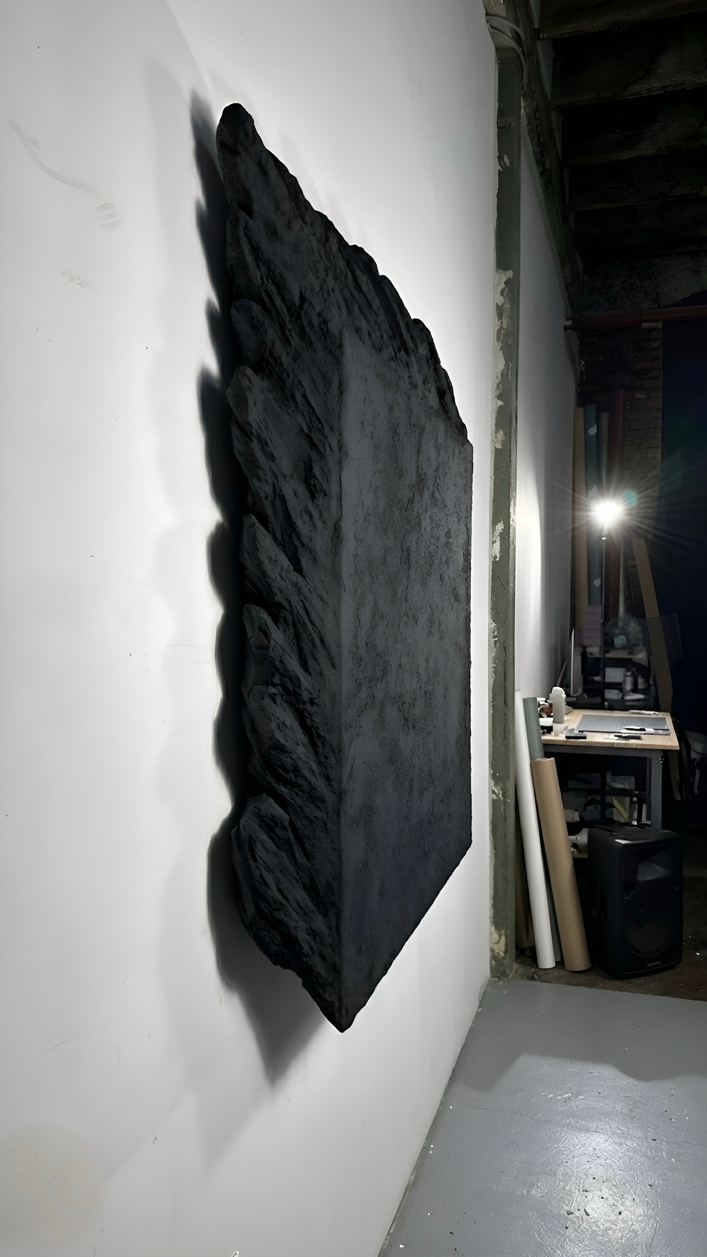 Large black textured artwork on a white wall in an indoor setting.