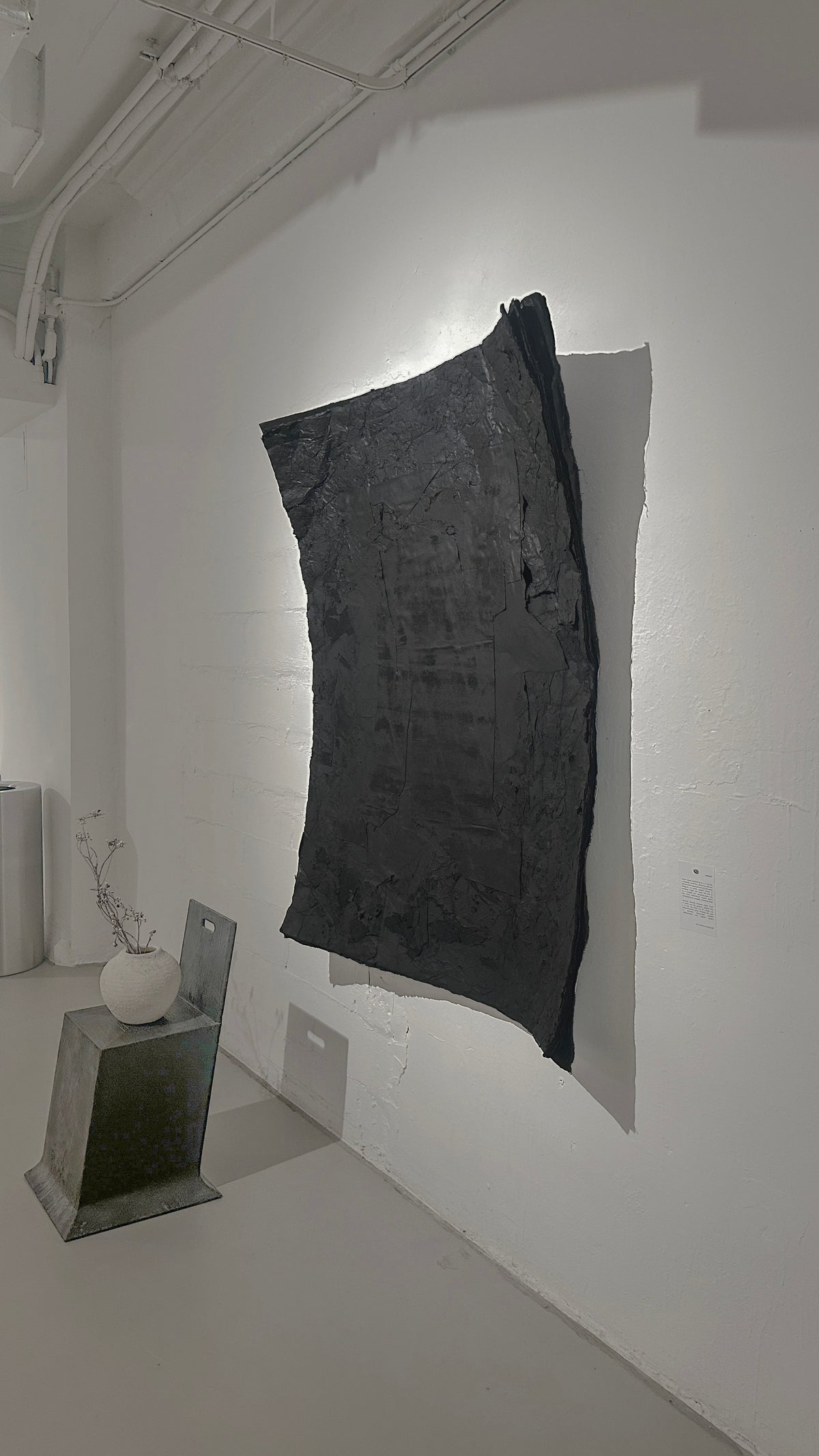 STRATA — Black, side angle in gallery beside a gray pedestal