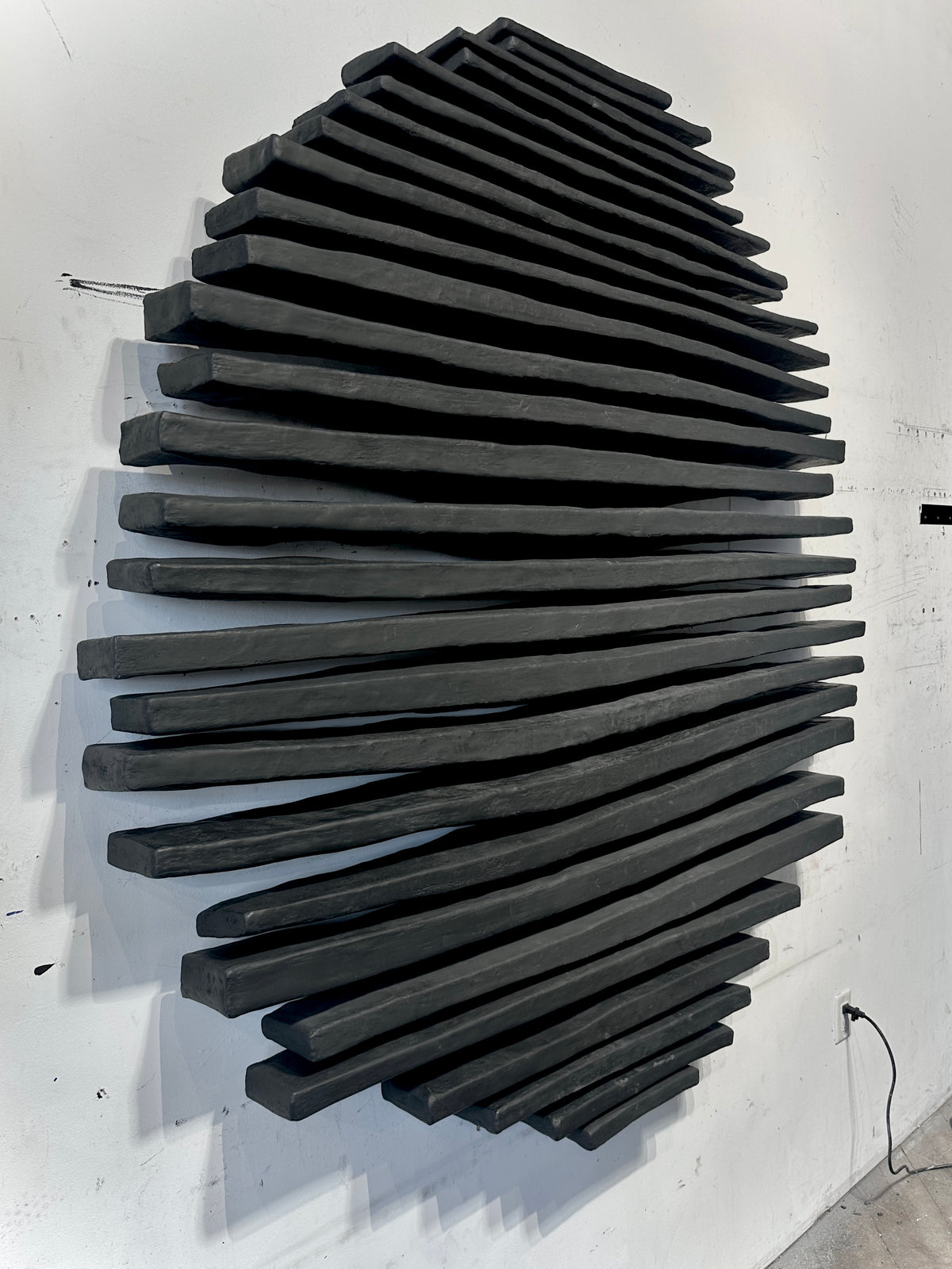 Black sculptural wall relief built from dense radiating rods, mounted on a white wall