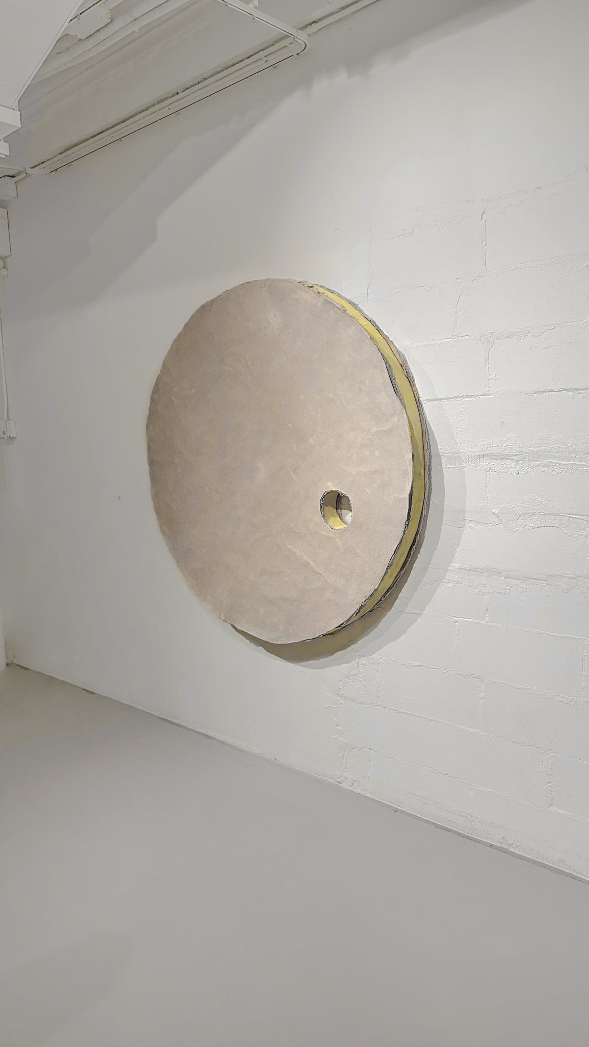 HELIOS — circular wall sculpture on white brick wall, angled view
