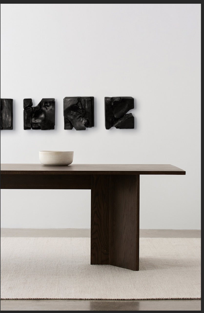 Modern dark wood dining table with a white bowl and abstract black wall art on a light gray background