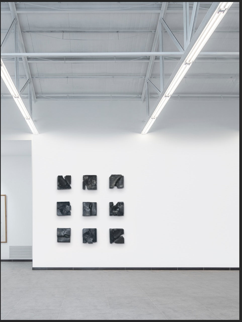 Nine black sculptures on a white wall in a gallery setting
