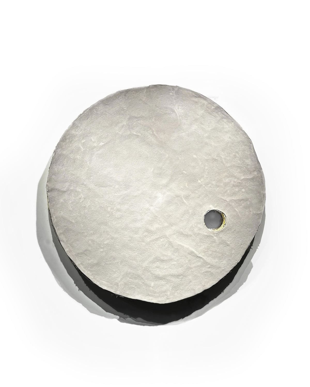 HELIOS — frontal view of round relief casting shadow on white wall