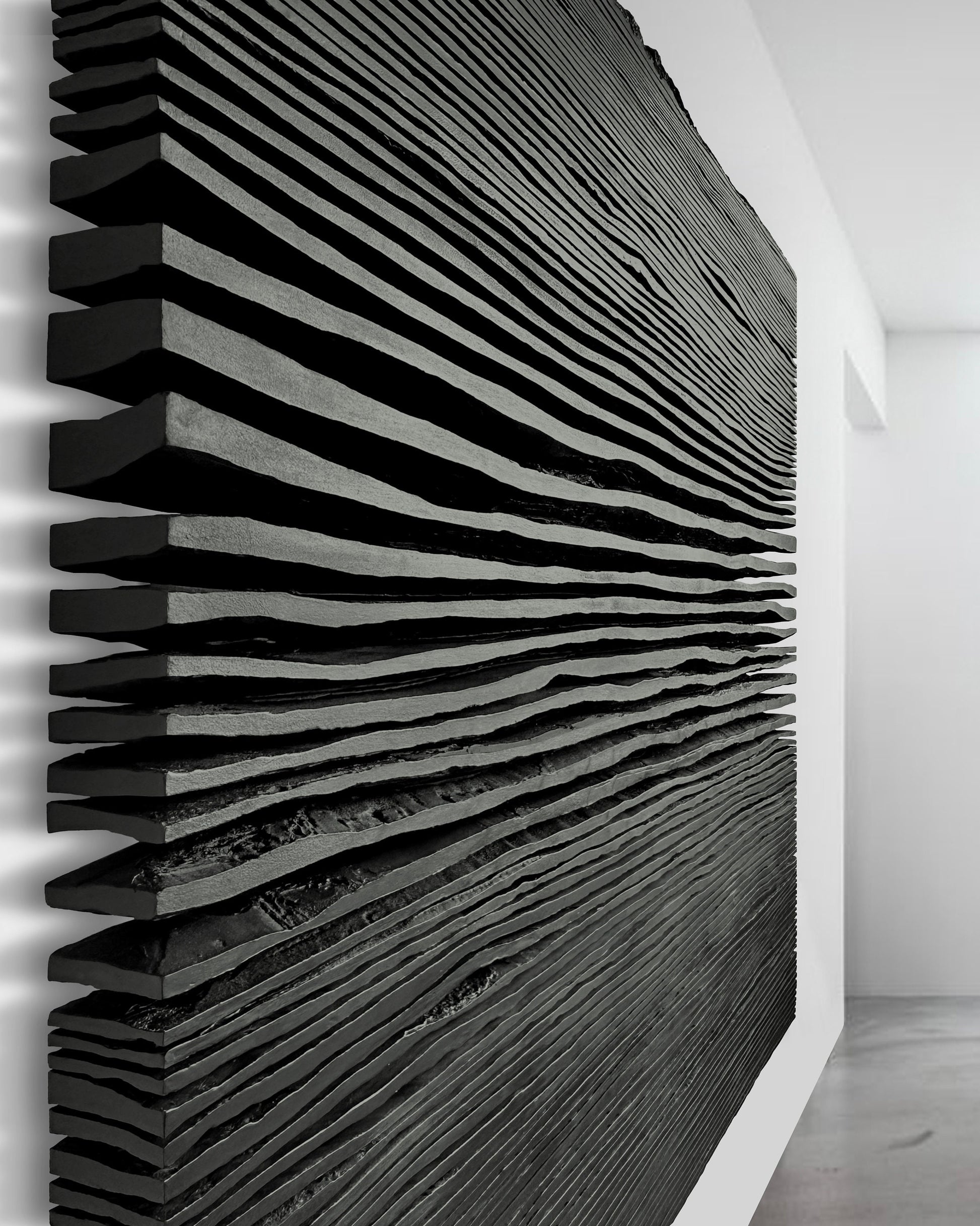 Matte black pleated plaster relief sculpture mounted above a console table in a sunlit living room with light wood floors.